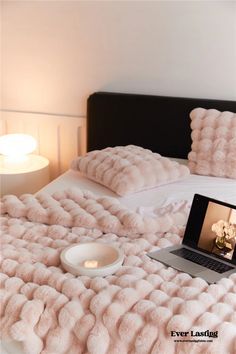 a laptop computer sitting on top of a bed covered in pink fluffy blankets and pillows