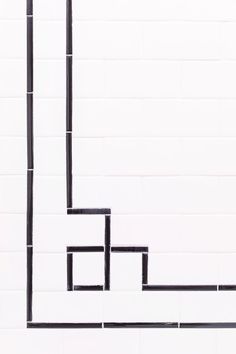 a white tiled wall with black lines in the center and one line going through it