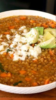 a white bowl filled with lentula soup and topped with avocado wedges