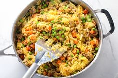 a pot filled with rice and vegetables on top of a counter next to a spatula