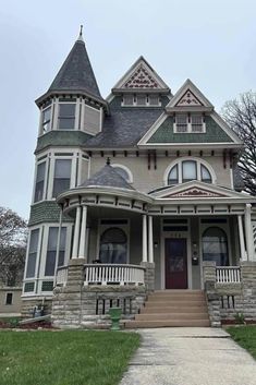 a large gray house with two stories and a turret on the second story, along with green grass