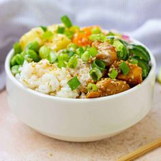 a white bowl filled with rice, meat and veggies next to chopsticks