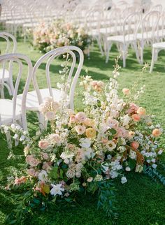 an outdoor ceremony with chairs and flowers on the grass, in front of rows of white lawn chairs