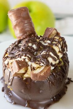 a chocolate covered dessert on a white plate with two green apples in the back ground