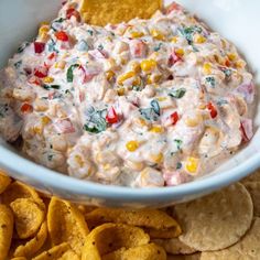 a white bowl filled with corn and dip surrounded by tortilla chips