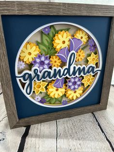 a shadow box with the word grandma surrounded by flowers and daisies in blue frame