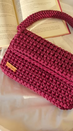 a crocheted purse sitting on top of a bed next to an open book