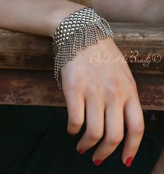 a woman's hand wearing a silver bracelet with chains on it and red nail polish