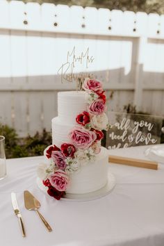 a wedding cake with pink and red flowers on it sitting on top of a table