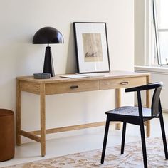 a desk with a chair, lamp and pictures on the wall next to it in a white room