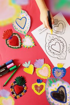 someone is making paper hearts with crayons and marker pens on a pink surface