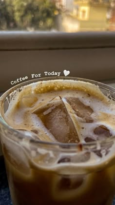 iced coffee in a glass cup with ice cubes on the rim, sitting next to a window