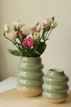 two green vases with pink and white flowers in them sitting on a round mat