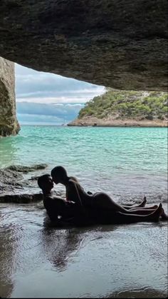 a woman laying on the ground next to a body of water with rocks in the background