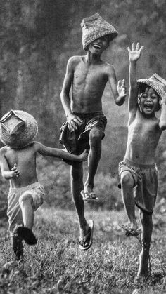 three young boys are running in the grass with hats on their heads and one boy is jumping