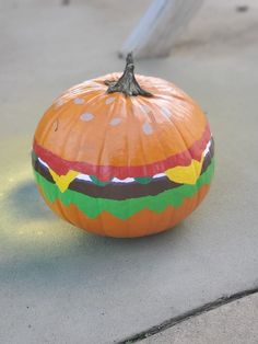 an orange pumpkin with a hamburger painted on it's side sitting on the ground