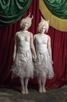 two women in white dresses standing next to each other with horns on their heads and hair