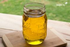 a jar filled with liquid sitting on top of a wooden cutting board next to a green field