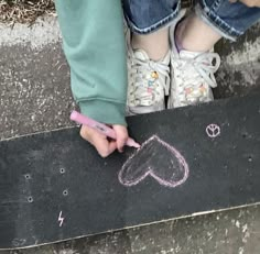 a person is writing on a skateboard with pink crayon pencils in front of them