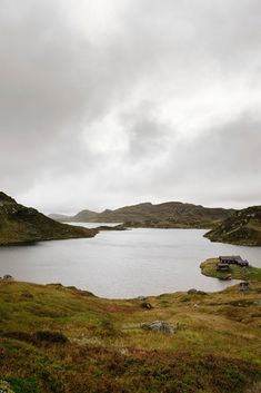 a large body of water surrounded by green hills and grass with a bench in the foreground