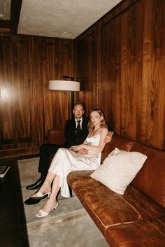 a man and woman sitting on a couch in a room with wood paneled walls