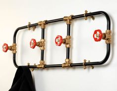 a coat rack made out of pipes with red and black knobs hanging on the wall