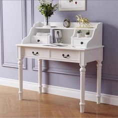 a white desk with two drawers and some books on it in front of a purple wall