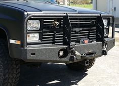 the front end of a black truck parked in a parking lot next to a building