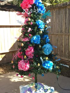 a small christmas tree decorated with blue, pink and red flowers in front of a fence