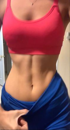 a woman in a red sports bra top and blue skirt is showing off her stomach