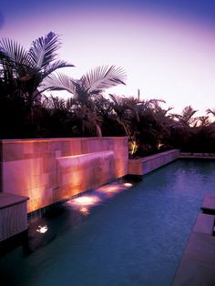 an outdoor swimming pool at night with lights on the wall and palm trees in the background