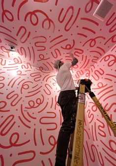 a man on a ladder painting the ceiling in a room with red and white designs