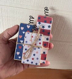 a hand holding a small gift wrapped in red, white and blue paper with twine