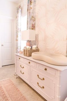 a white dresser sitting in a bedroom next to a wallpapered wall with pink flowers on it