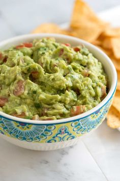 a white bowl filled with guacamole surrounded by tortilla chips