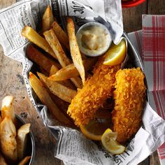 fried fish and french fries in a basket with lemon wedges on the side next to dipping sauce