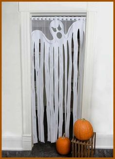 two pumpkins sitting on the floor next to a white curtain with ghost decorations hanging from it