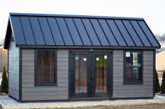 a small gray shed with two windows and a black roof