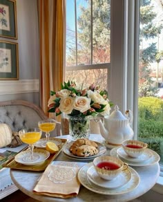 the table is set with tea, pastries and flowers in front of a window