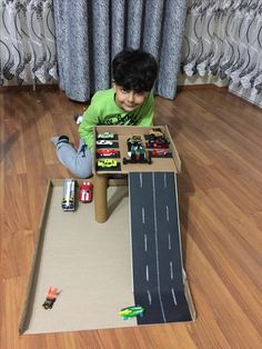 a young boy playing with toy cars in a cardboard box