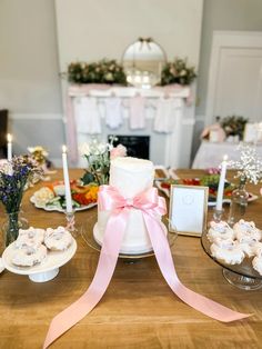 a table topped with cakes and cupcakes covered in pink ribbon next to candles