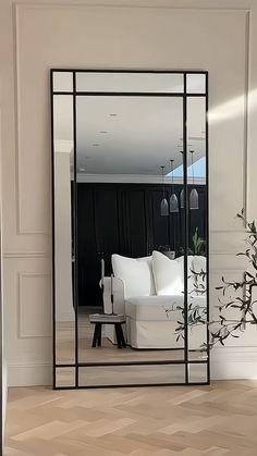 a large mirror sitting on top of a wooden floor next to a white couch and table