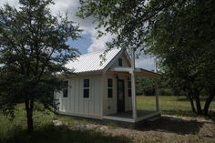 a small white building sitting in the middle of a field next to trees and grass