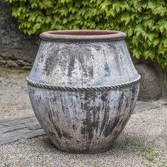 a large pot sitting on top of a stone floor next to a planter filled with green leaves