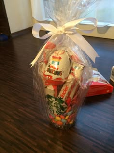 a starbucks cup filled with candy and wrapped in cellophane on top of a wooden table