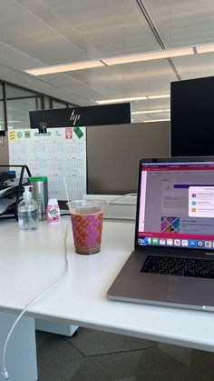 an open laptop computer sitting on top of a white desk next to a cup of coffee