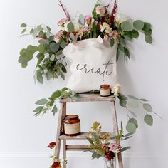 a white bag sitting on top of a wooden step ladder next to flowers and candles