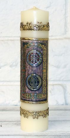 a lit candle with an ornate design on the front and sides, sitting on a white surface