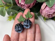 a person holding two small blackberries in their hand next to pink flowers and green leaves