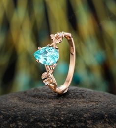 a gold ring with blue topazte and diamond accents on a rock in front of trees